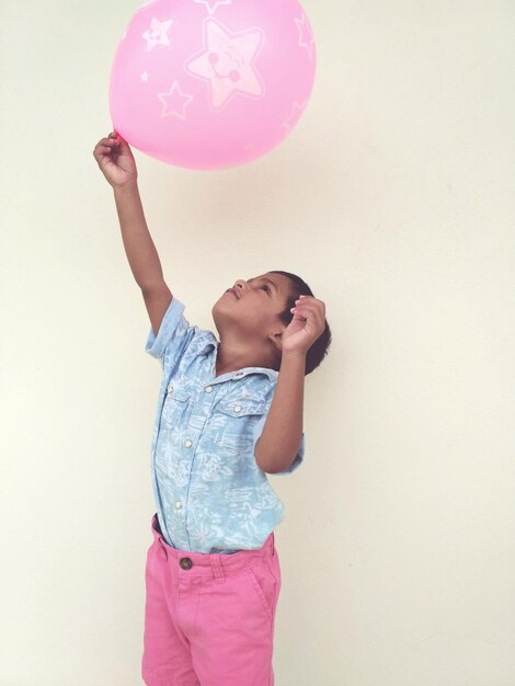 Photo un garçon tenant un ballon rose contre le mur.