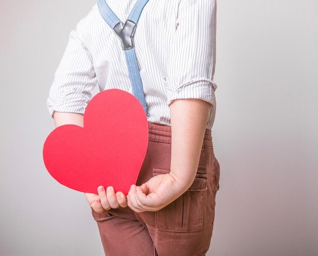 Garçon tenant un coeur rouge derrière le dos