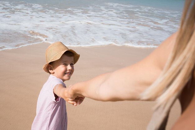 Garçon tenant la main de sa mère sur la plage et demandant à le suivre