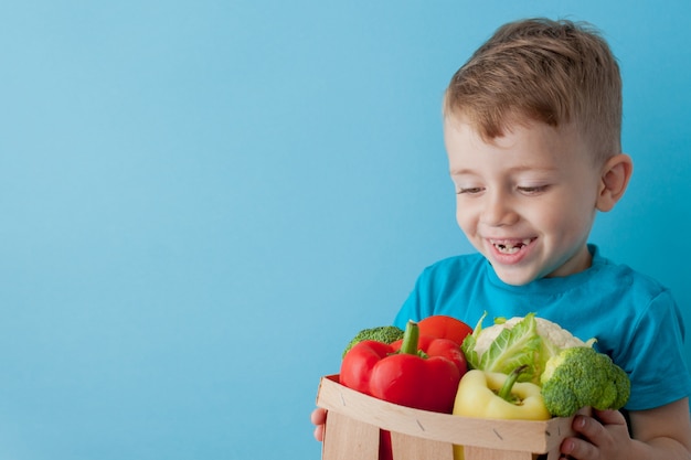 Garçon tenant un panier avec des légumes frais sur fond bleu. Concept végétalien et sain.