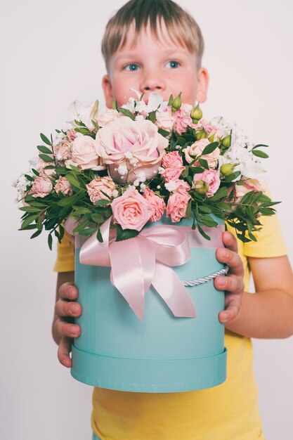 Le garçon tient une composition florale dans une boîte ronde. Un cadeau pour maman. Garçon avec un bouquet de fleurs. Teinture vintage.