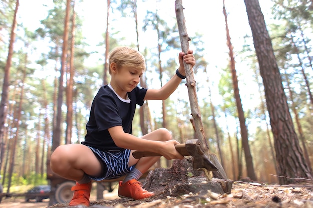 Le garçon tient une hache dans une main et un bâton dans l'autre et le coupe pour le bois de chauffage