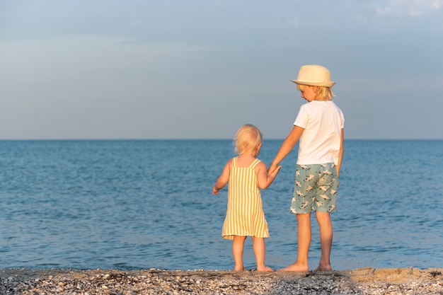 Le garçon tient la petite fille par la main au bord de la mer. Enfance insouciante.