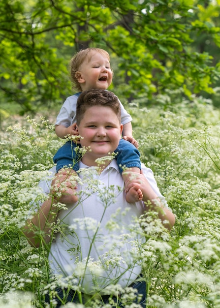 un garçon tient sur ses épaules un enfant riant joyeusement avec des cheveux blonds ondulés d'un an