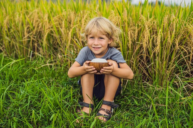 Le garçon tient une tasse de riz bouilli dans une tasse en bois sur le fond d'un champ de riz mûr. Concept de nourriture pour enfants.