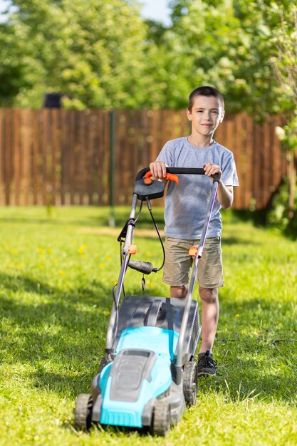 Garçon travailleur sur le jardin travaillant à tondre la pelouse à l'aide d'une tondeuse à gazon moderne