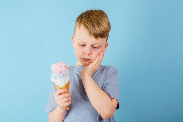 Un garçon triste attrapa sa joue ressentit un mal de dents aigu L'enfant tenant de la crème glacée dans sa main