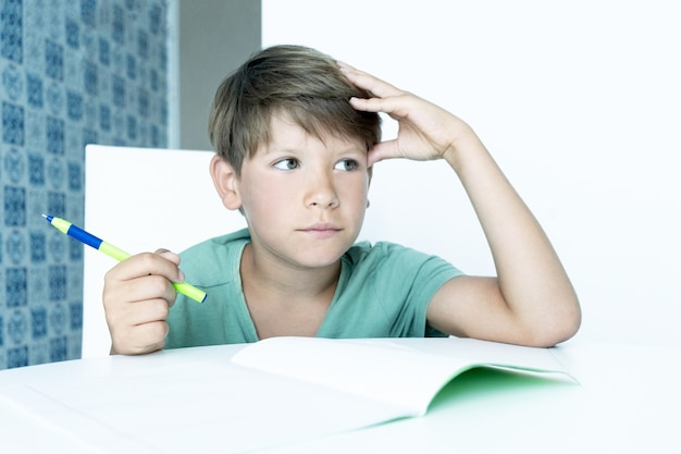 Un garçon triste avec un livre fait ses devoirs à l'école. Retour à l'école. Écolier malheureux avec des manuels. Apprentissage à distance.
