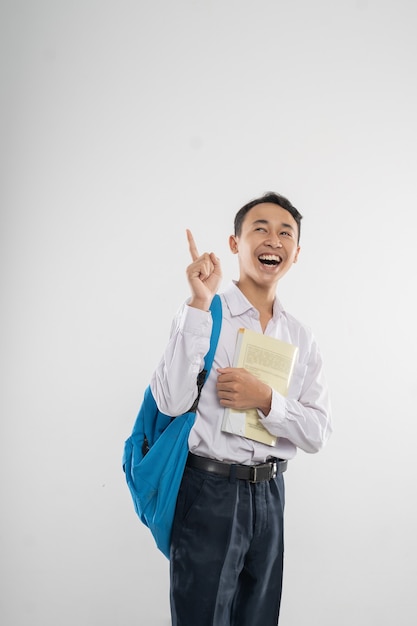 Un garçon en uniforme de lycée regardant avec le doigt pointé lorsqu'il porte un livre et un backp...