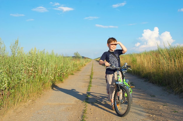 Le garçon avec un vélo sur une longue route