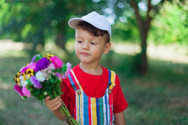 Photo un garçon en vêtements lumineux avec des fleurs dans ses mains sur fond de parc naturel