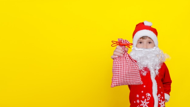 garçon en vêtements de père Noël barbe blanche montre un sac de cadeaux sur sa main tendue mise au point sélective