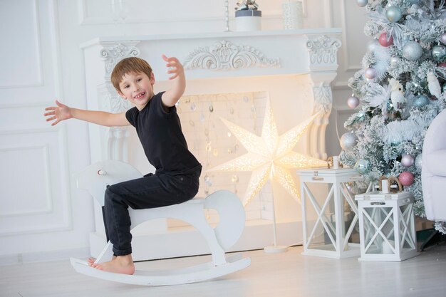 Un Garçon En Vêtements Sombres Sur Un Cheval Jouet Dans La Salle Du Nouvel An Joyeux Enfant à Noël à La Maison