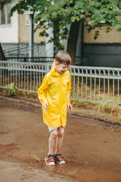 Un garçon vêtu d'un imperméable jaune sort sous la pluie. Un enfant saute sur le passage. sauter à travers des flaques boueuses. Enfance heureuse et insouciante