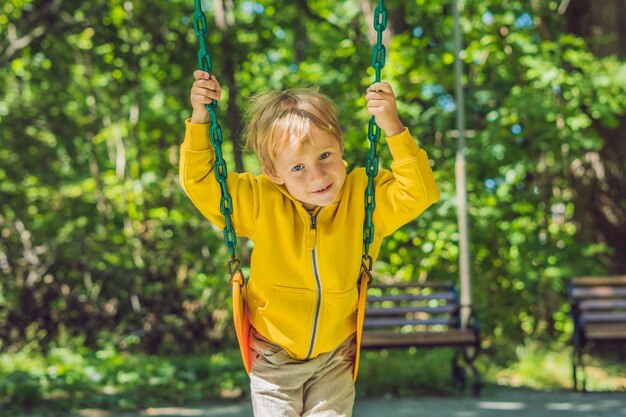 Un garçon vêtu d'un sweat-shirt jaune est assis sur une balançoire sur une aire de jeux en automne