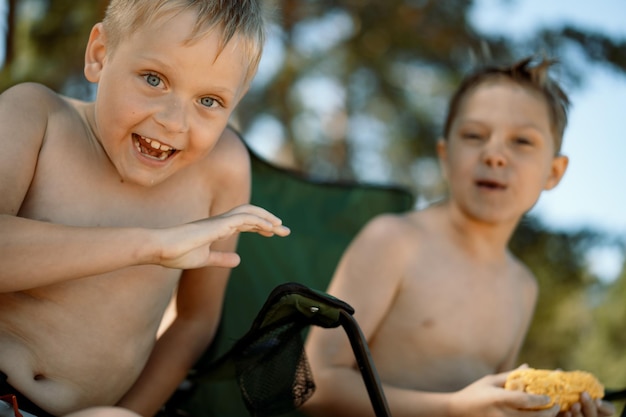 Garçons caucasiens mignons assis sur la plage de maïs assis sur des chaises de camping en riant profiter de vacances