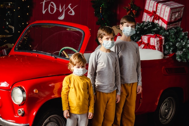 Garçons de frères sérieux mignons dans des masques médicaux debout près de la voiture de Noël.