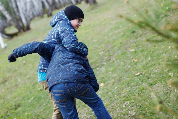 Les garçons jouent sur la pelouse verte. Un adolescent avec un chapeau noir et des lunettes se débat avec son ami sur l'herbe verte.