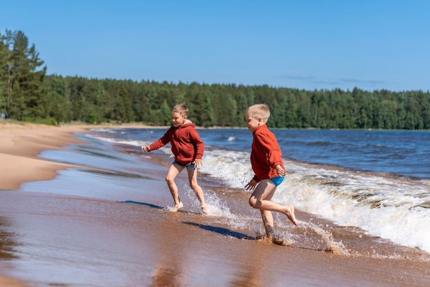 Garçons mignons portant des sweats à capuche rouges et des sous-vêtements bleus courant des vagues dans le lac Ladoga