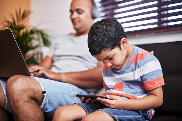 Les garçons sont en mode travail Photo recadrée d'un petit garçon insouciant naviguant sur une tablette numérique pendant que son père travaille sur son ordinateur portable sur le canapé à la maison pendant la journée