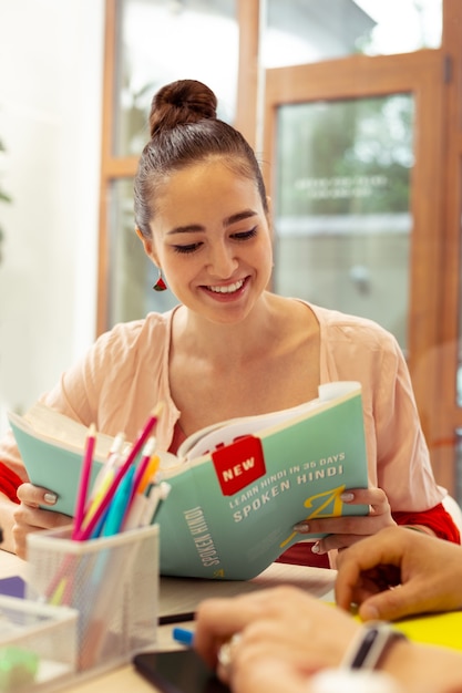 Garder le sourire. Charmante jeune femme exprimant sa positivité tout en apprenant une nouvelle langue