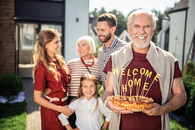 Garder le sourire. Heureux retraité tenant le gâteau dans les deux mains en attendant les invités