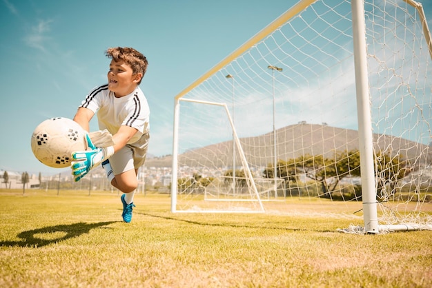 Gardien de but de garçon de football et ballon de sauvetage de saut des buts sur le terrain de sport en plein air Enfant de football et jeu de compétition avec gardien de but de fitness et ballon de football sur l'herbe succès et action pour sauver le but