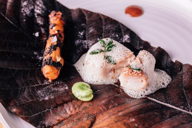 Garniture de poisson avec de la mousse sert de pois et de racine grillée avec du sel sur une feuille incendiée