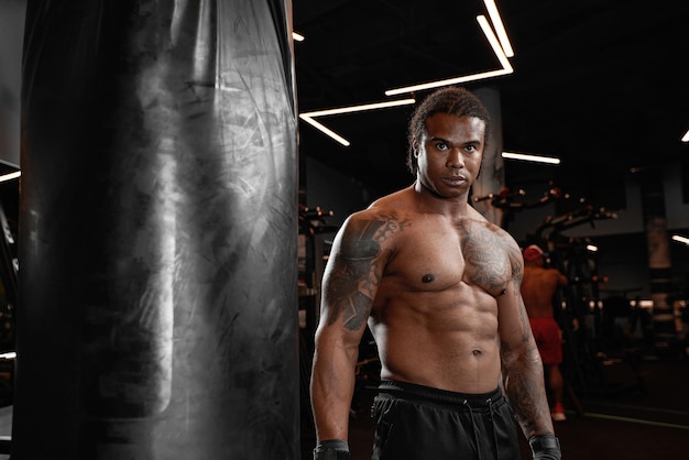 Un gars afro-américain s'entraîne dans une salle de sport et poings ses poings de sac de boxe Concept de gym fitness boxe succès entraînement et puissance