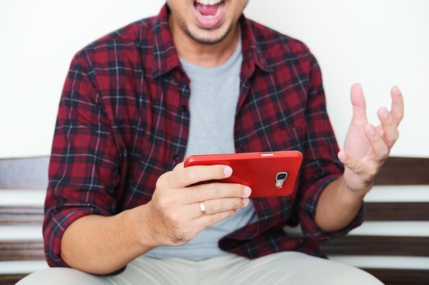 Un gars assis sur un banc jouant à un jeu mobile et montrant un geste de rage