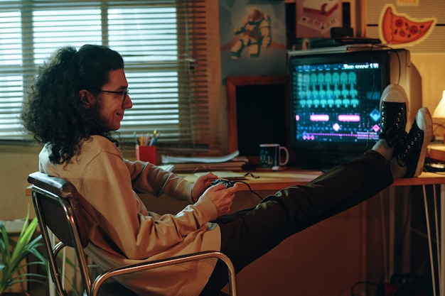 Un gars assis sur une chaise et jouant à une console de jeux vidéo pendant son temps libre