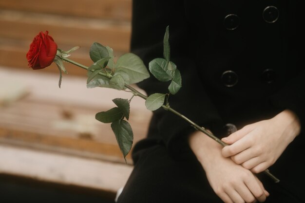 Photo un gars attend une fille à un rendez-vous un garçon dans un manteau noir avec une fleur de rose