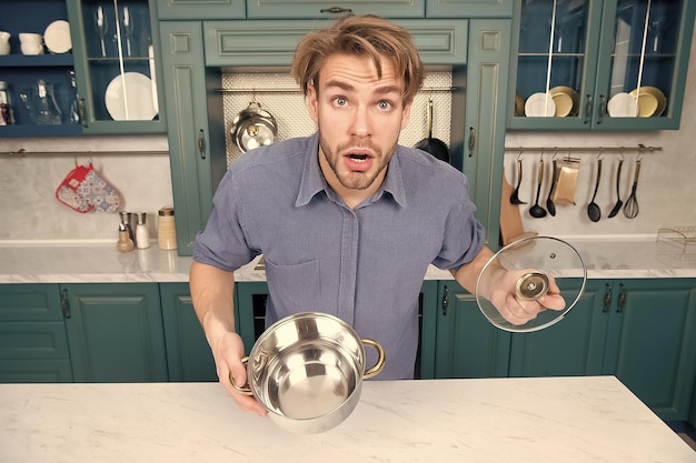 Un gars au visage surpris tient le couvercle de la casserole ouvert dans la cuisine