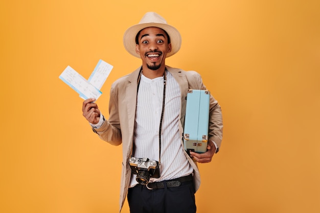 Le gars aux yeux bruns est heureux de ses futures vacances, détient des billets et une valise. L'homme charmant aime le voyage