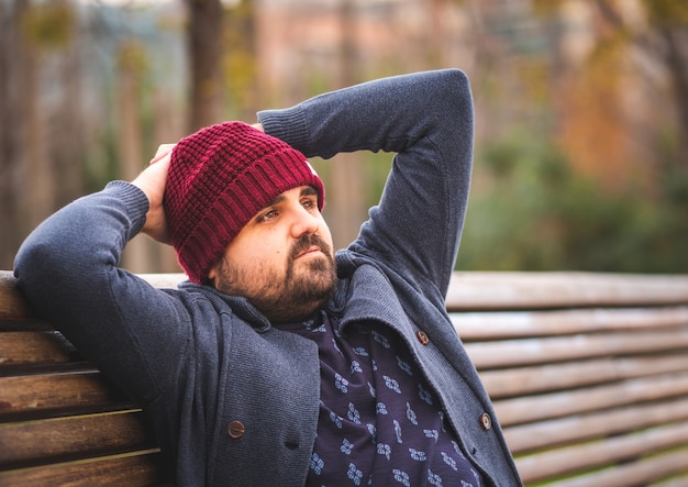 Gars à bord dans un chapeau de laine et un pull assis sur un banc de parc de détente