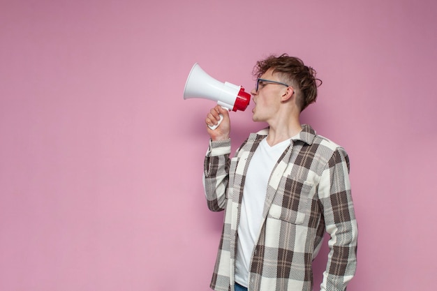 Un gars bouclé avec des lunettes crie fort dans un mégaphone une annonce sur fond rose