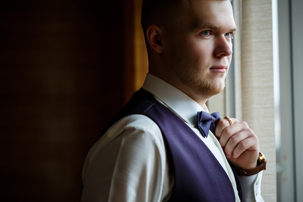 Un gars en chemise blanche et pantalon s'habille le jour d'un mariage.