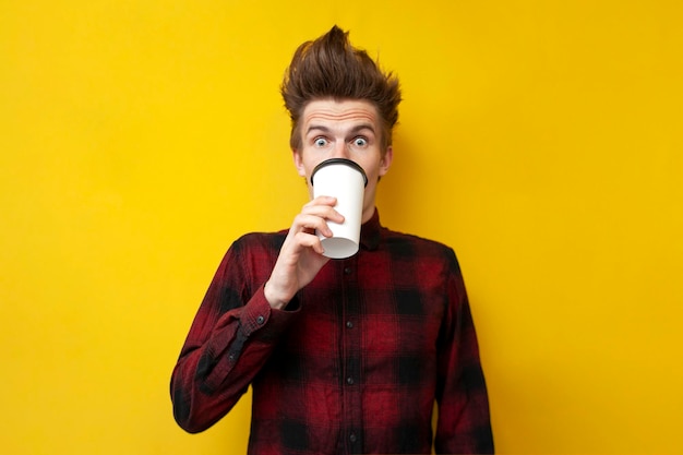 Un gars choqué boit du café revigorant et est surpris par un fond jaune isolé un homme boit une boisson énergisante