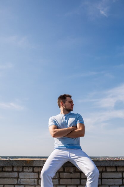 Un gars cool attirant dans un T-shirt bleu avec une barbe est assis sur le fond du ciel bleu.