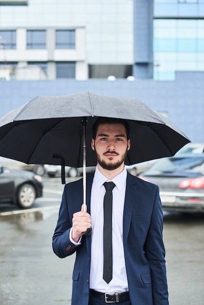 Le Gars En Costume Sur Le Parking Avec Un Parapluie à La Main