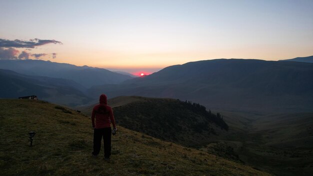 Un gars dans les montagnes regarde le coucher du soleil