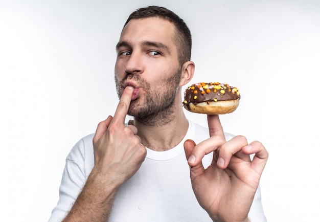 Un gars dans un T-shirt blanc tient un beignet au chocolat sur son doigt