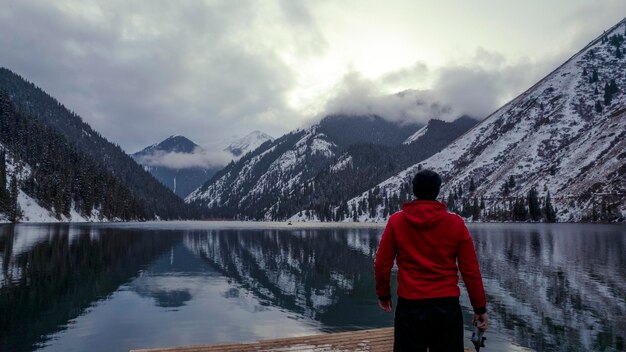 Le gars debout sur la jetée admire le lac de montagne. Il offre une vue sur le paysage