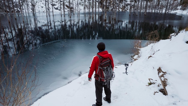 Un gars debout sur le rivage admire un lac de montagne. L'eau reflète la forêt comme un miroir.