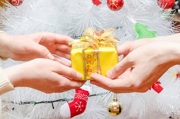 Le gars donne un cadeau à la fille contre le sapin de Noël blanc. Moment joyeux