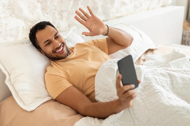 Un gars du Moyen-Orient faisant un appel vidéo par téléphone dans la chambre