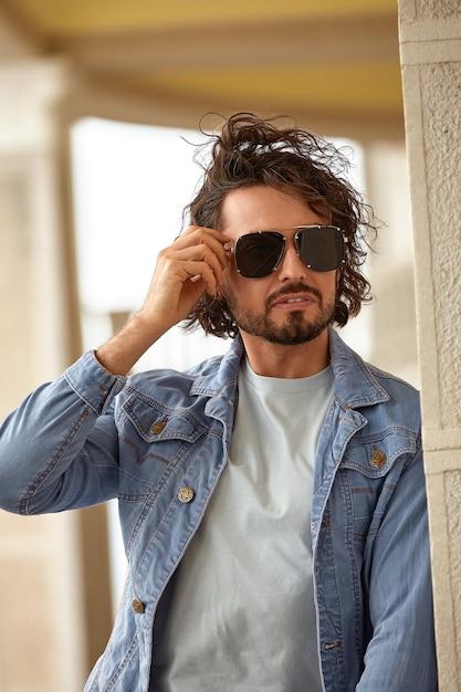 Un gars élégant avec des lunettes mur de pierre sur le fond et regarde loin un homme fort et strict dans des vêtements décontractés