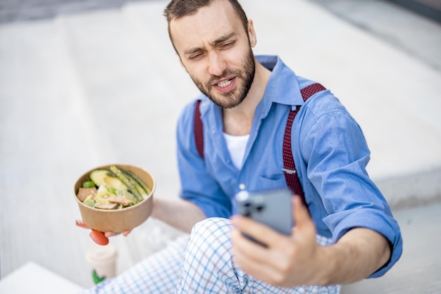 Un gars élégant mange des plats sains à emporter au travail à l'extérieur