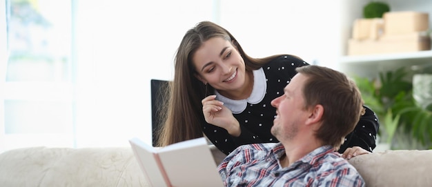 Le gars est assis sur le canapé avec le livre la fille sourit