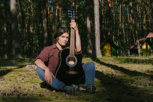 Le gars est assis avec une guitare dans les bois. Dans le contexte du camp forestier.